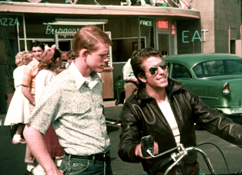 Henry Winkler as The Fonz in a leather jacket and sunglasses on a motorcycle, with Ron Howard standing next to him outside a diner.