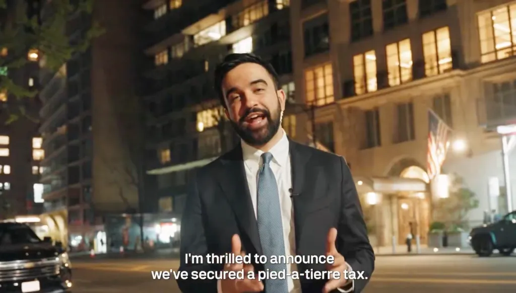 A man in a suit standing on a city street at night announces a pied-à-terre tax.