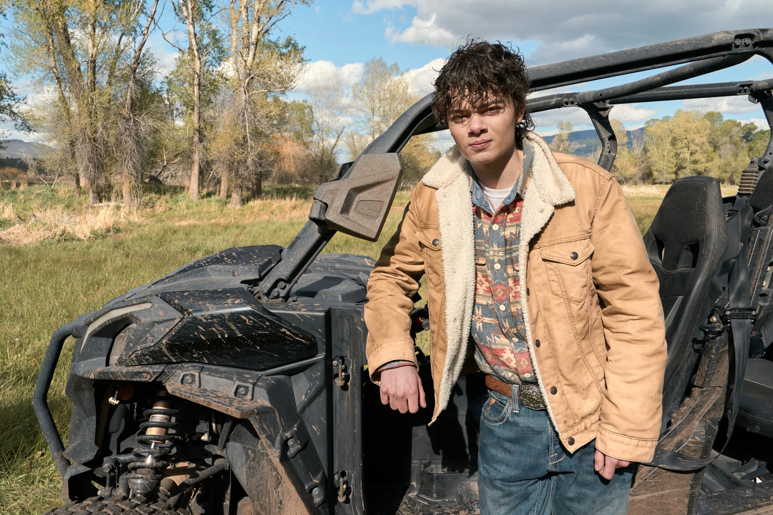 Brecken Merrill as Tate Dutton leaning against a muddy ATV in an outdoor field.
