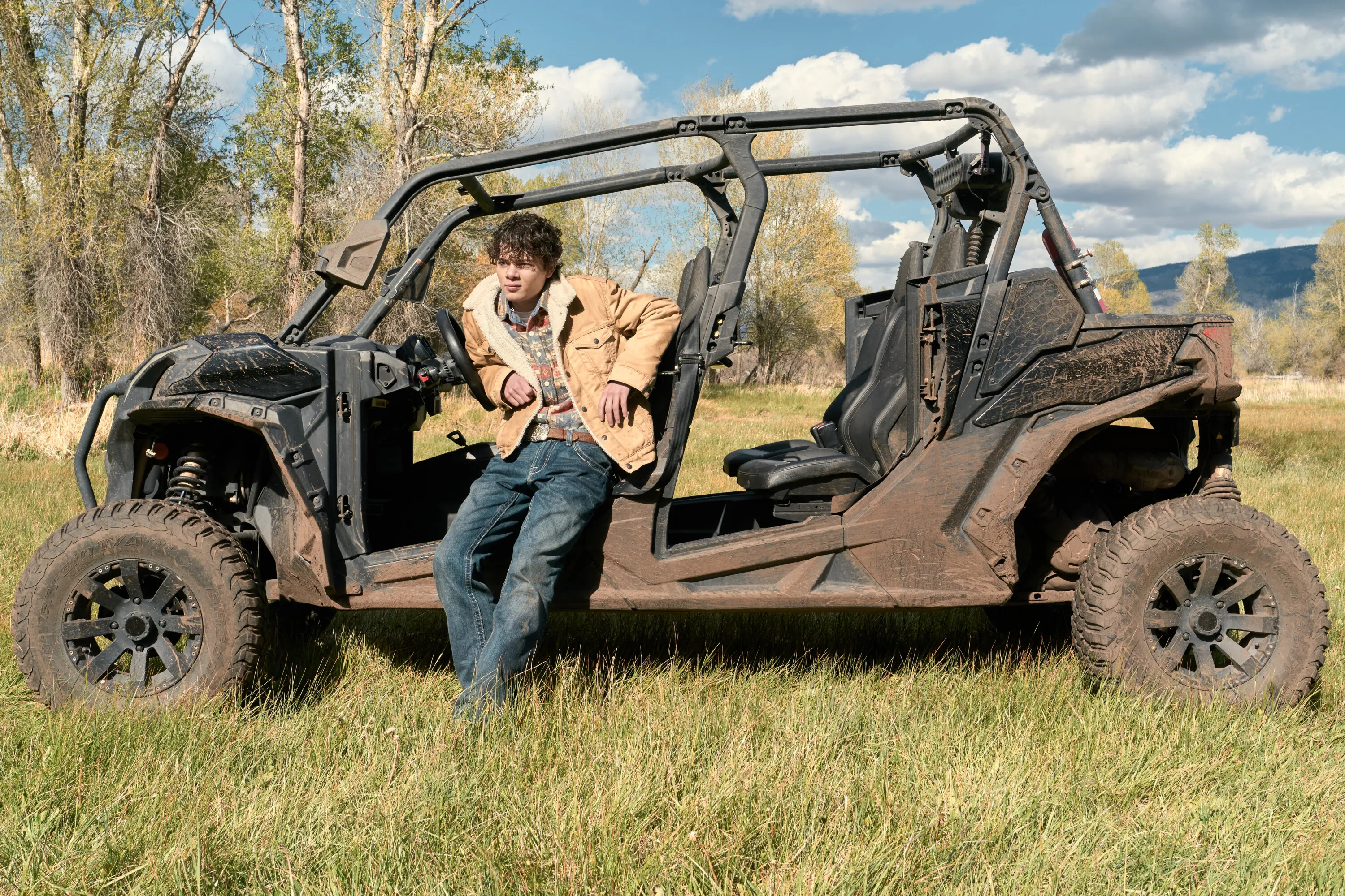 Brecken Merrill as Tate Dutton leaning against a muddy ATV in a grassy field.