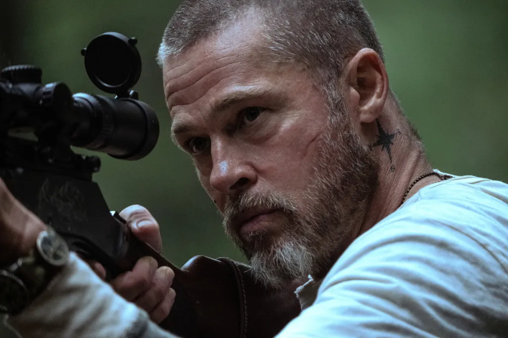 Brad Pitt, in a grey top, as a character holding a rifle in 