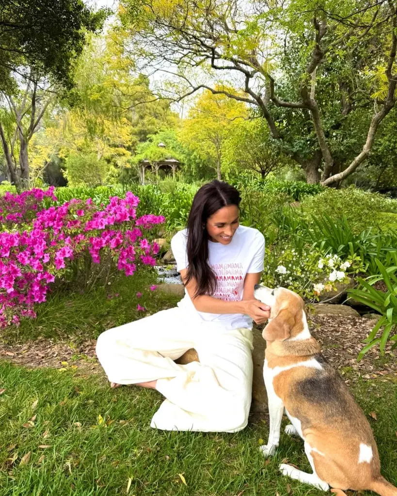 Meghan Markle sits in a lush garden next to a beagle, gently petting its chin.