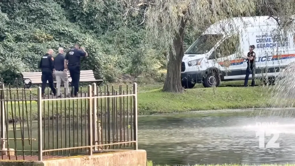 Police officers and a Nassau crime scene search unit van are stationed at a park near a body of water where human remains were discovered.