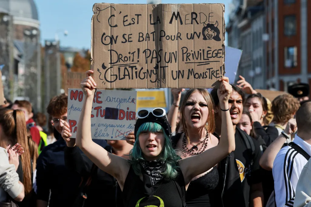 A person holds a cardboard placard with French text during a student protest in Liege.