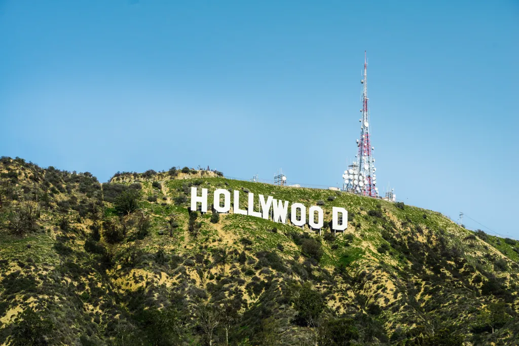 The Hollywood sign on a green hillside with a tall communications tower against a blue sky.