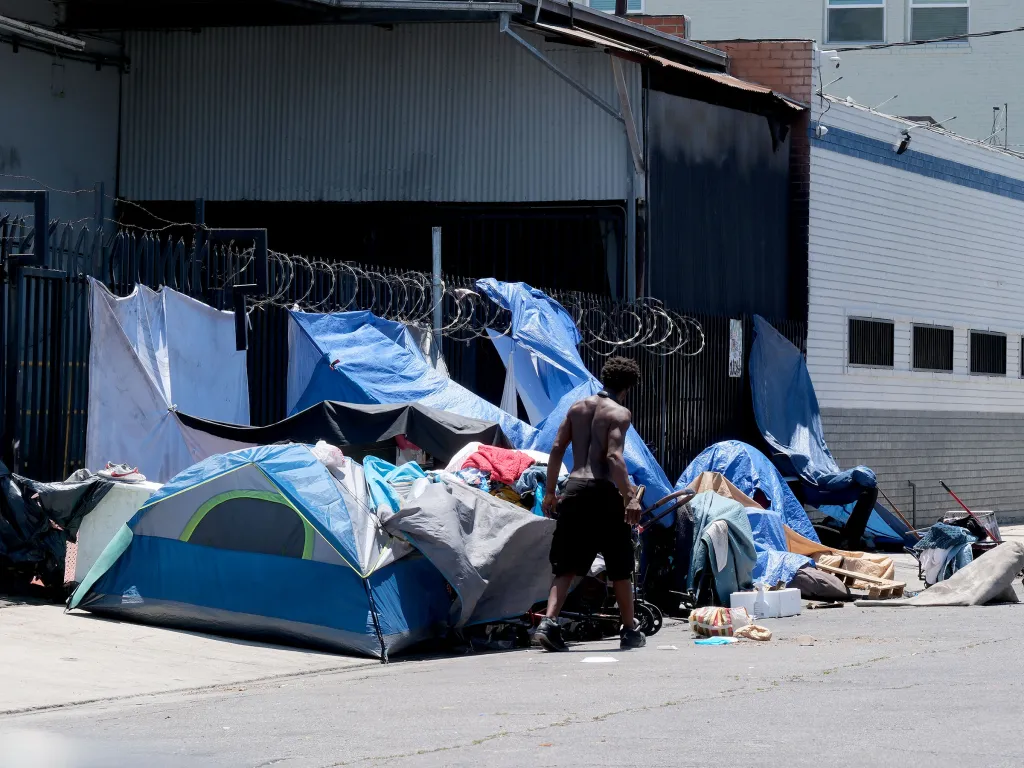 A homeless encampment with tents and tarps set up on a sidewalk in downtown Los Angeles.