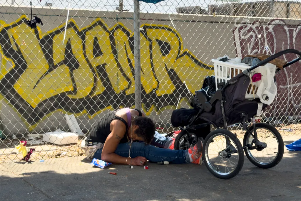 Homeless person sitting on the ground next to a stroller on Skid Row.