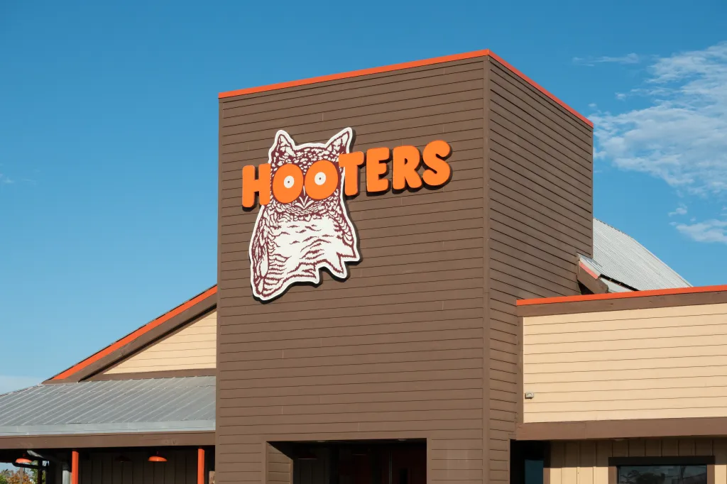 Exterior of a Hooters restaurant featuring the trademark owl logo against a clear blue sky.