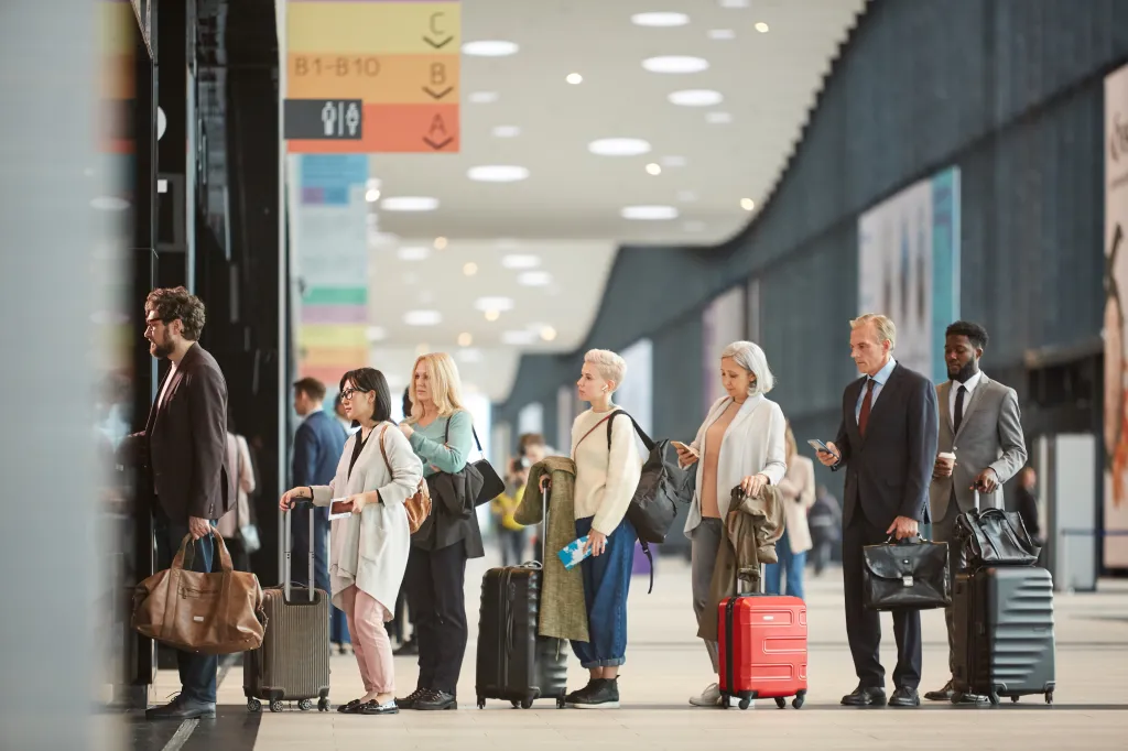 A side view of people with their luggage waiting in a queue at airport customs.