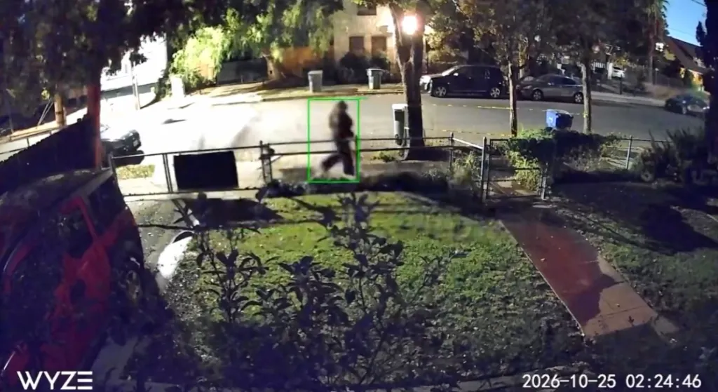 A surveillance camera still showing a person walking near a street outside a house at night, highlighted by a green box.