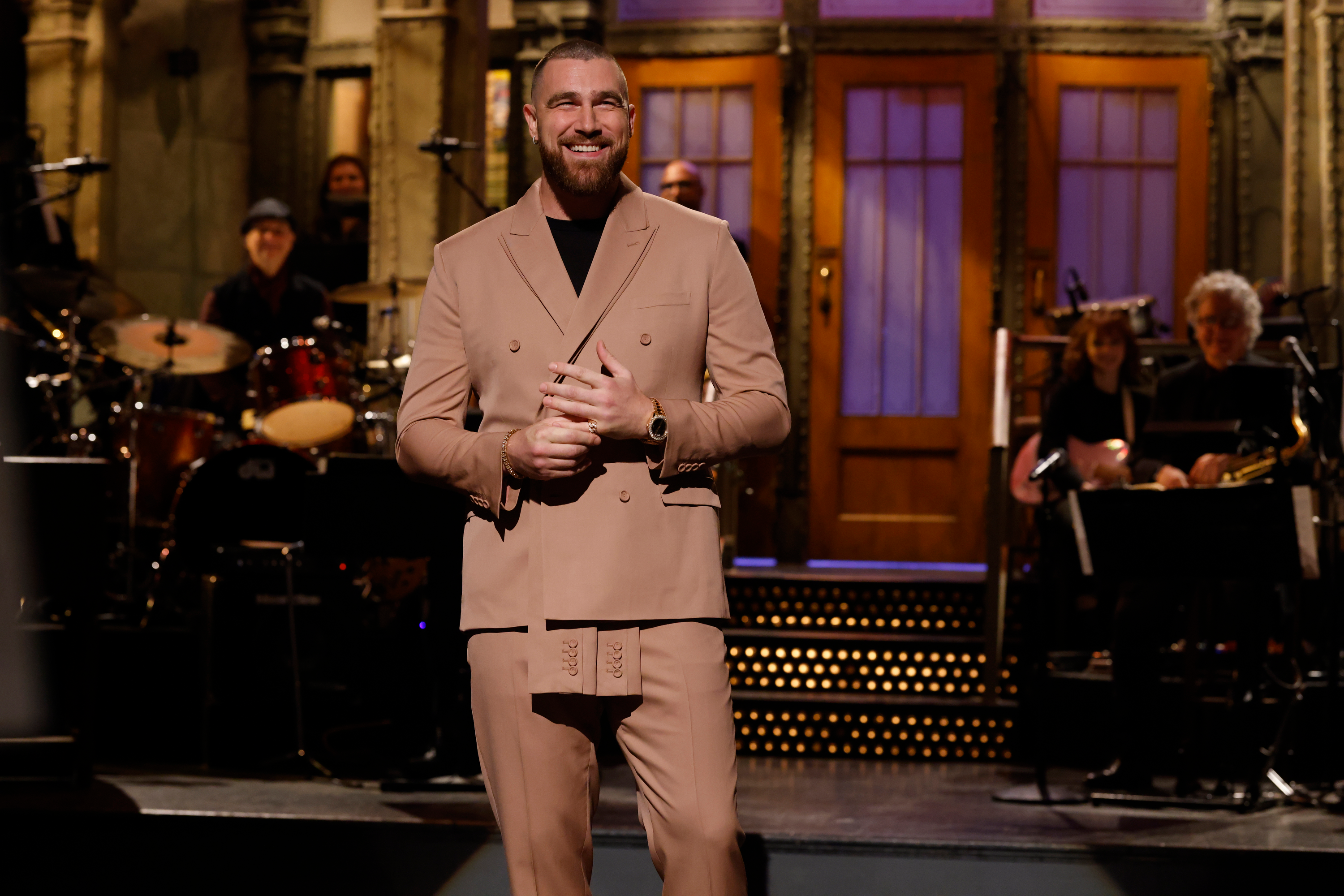 Travis Kelce smiling on the Saturday Night Live stage during his monologue.