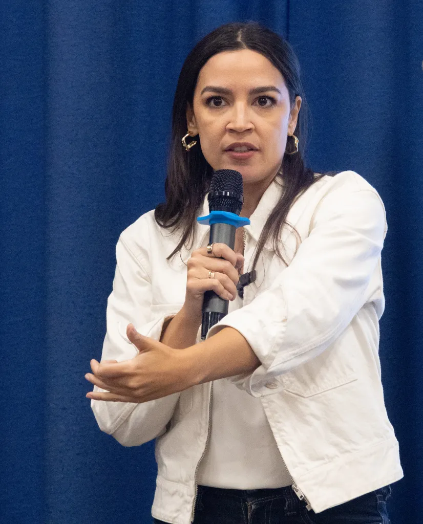 Rep. Alexandria Ocasio-Cortez speaks into a microphone while gesturing during a town hall in Queens.
