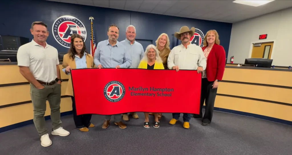 A group of people standing behind a banner for Marilyn Hampton Elementary School.