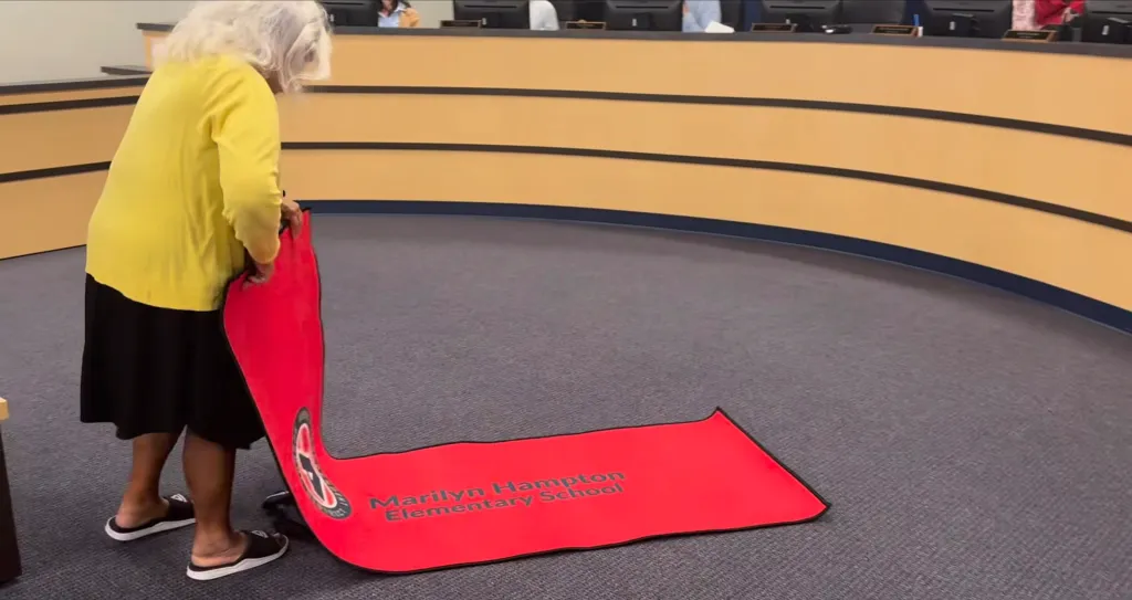 Retired custodian Marilyn Hampton unrolls a red mat bearing the name of her namesake elementary school.
