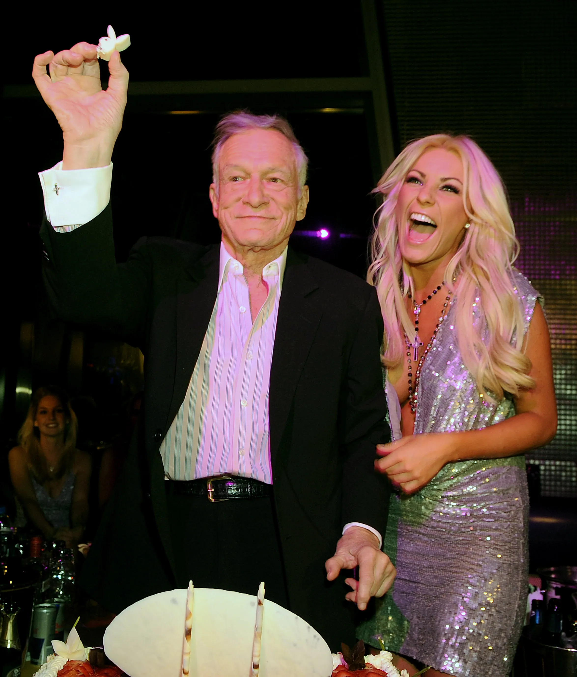 Hugh Hefner and Crystal Harris holding up a Playboy bunny cake topper at his birthday party.