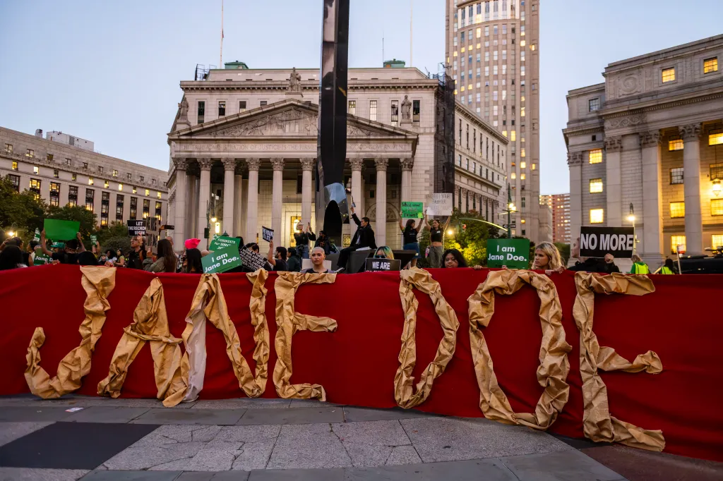 A crowd of demonstrators hold a large red banner reading