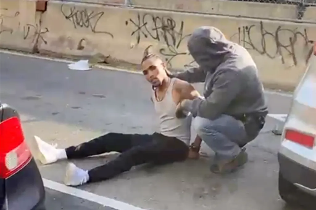 A person sits injured on the ground while another person in a hooded sweatshirt kneels next to them during an ICE-related encounter in the Bronx.