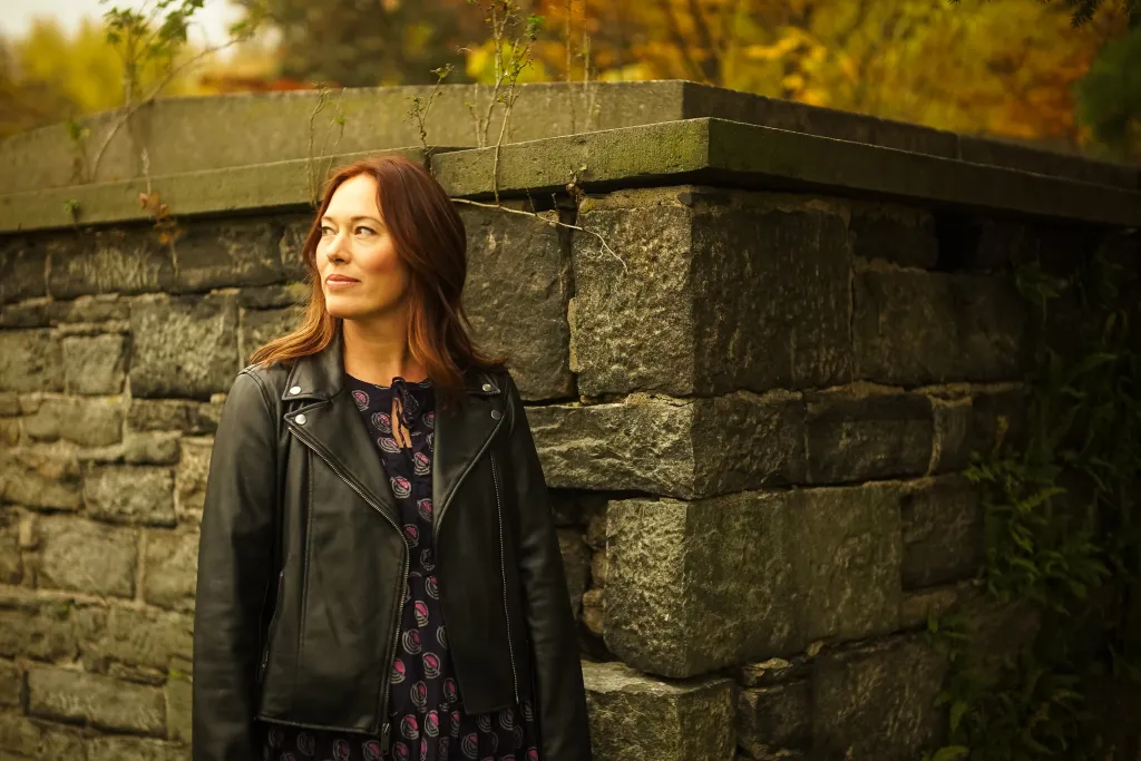 Andrea Janes wearing a black leather jacket in front of a stone wall.