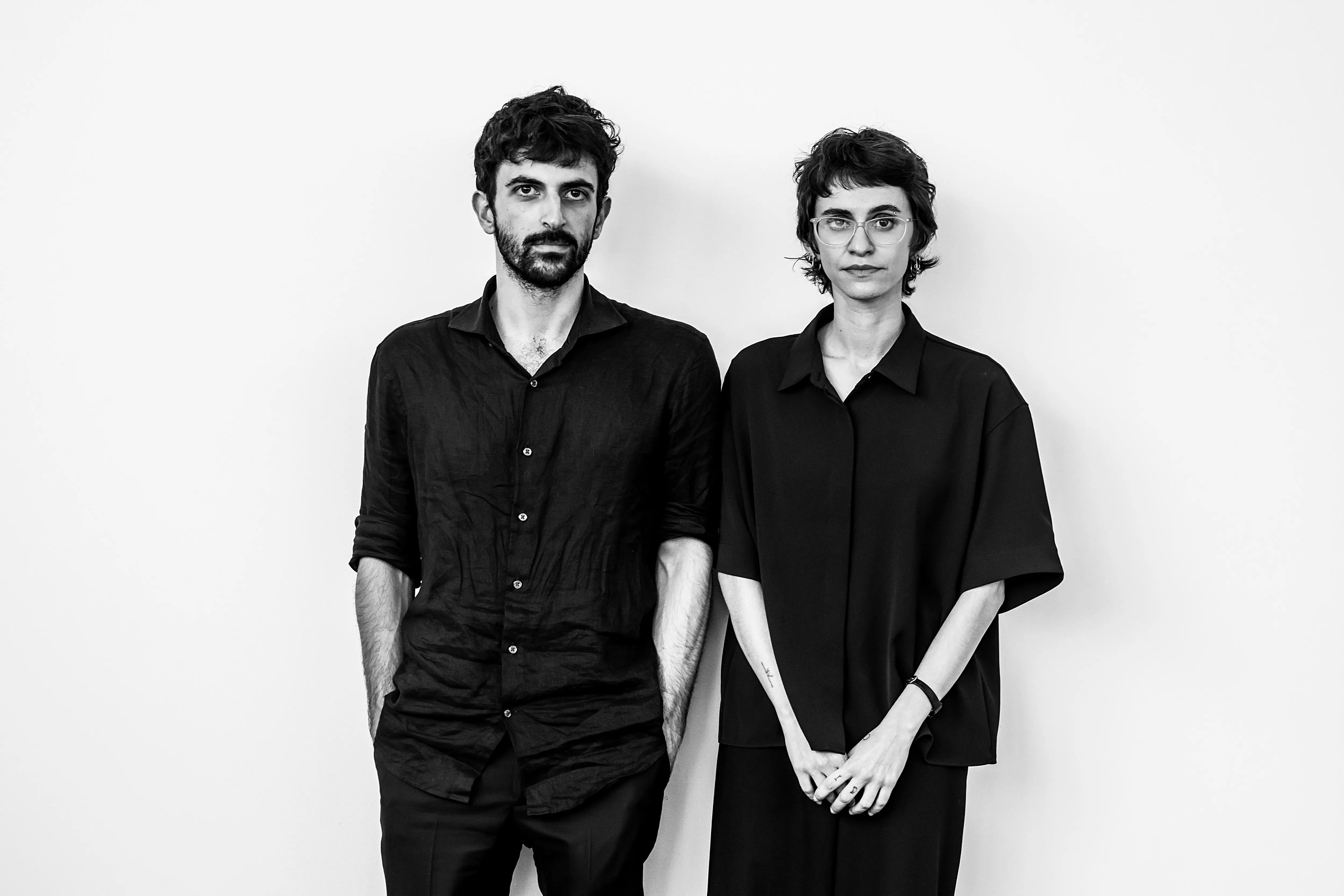 Black and white portrait of filmmaker Yuval Abraham and journalist and director Rachel Szor standing together against a plain background.
