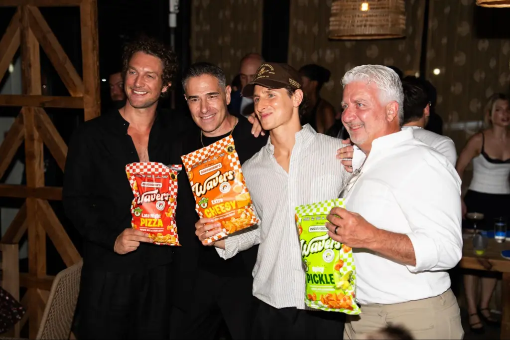 Four men holding bags of Doughbies's snack chips in an indoor setting.