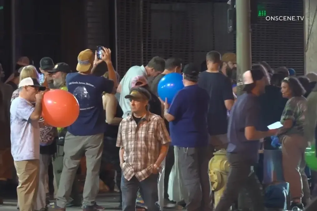 People stand alongside nitrous oxide (NOS) tanks while inhaling from balloons on a block in Los Angeles.