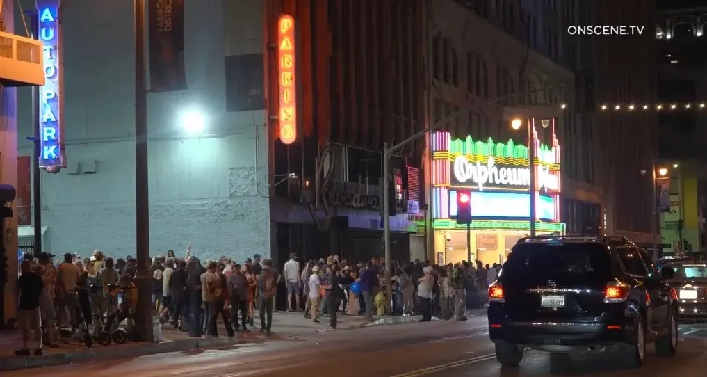 People stand alongside nitrous oxide (NOS) tanks while inhaling from balloons on a city block at night.