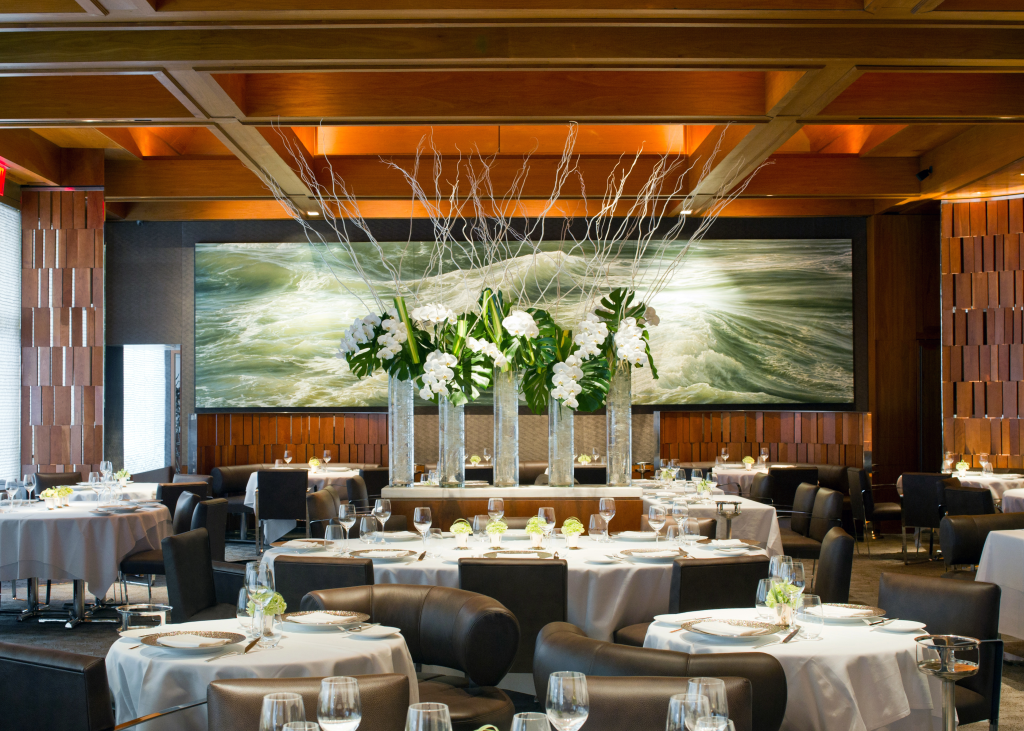 Interior of Le Bernardin restaurant, featuring elegant dining tables and a large floral arrangement in the center.