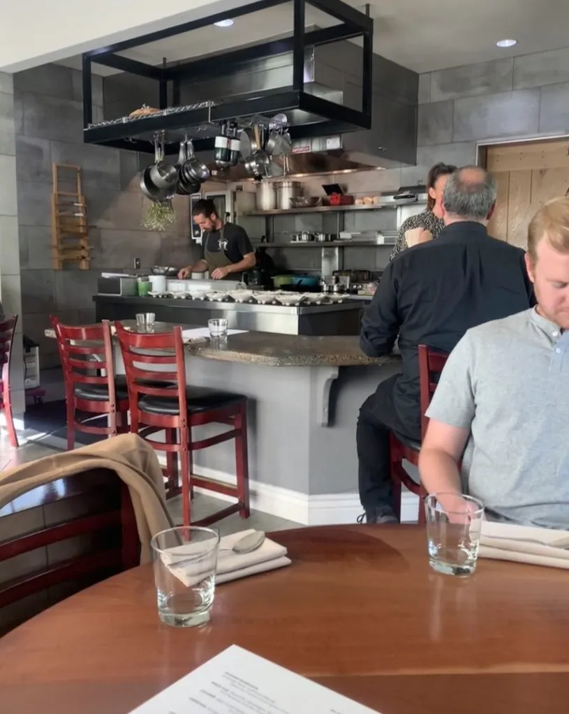 Interior view of Michael Warring restaurant with customers seated at tables and a chef working in the open kitchen.