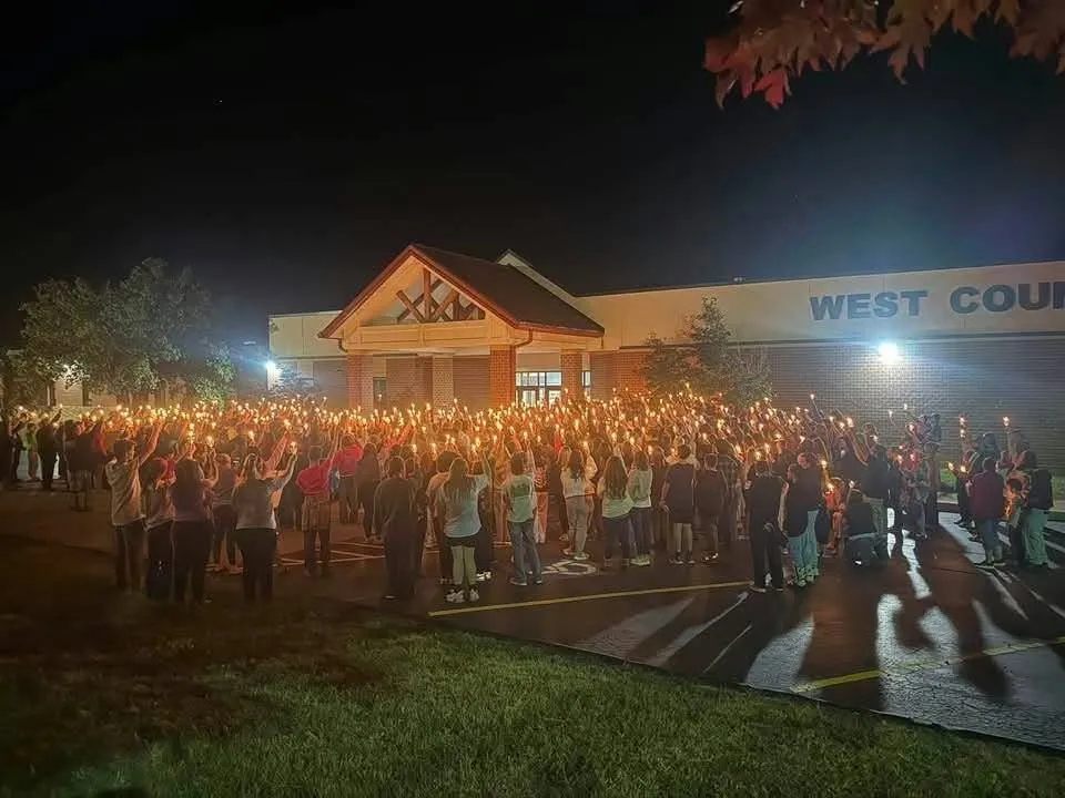 Community members hold a candlelight vigil outside West County High School at night.