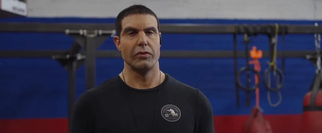 Sacha Baron Cohen in a black shirt in a gym.