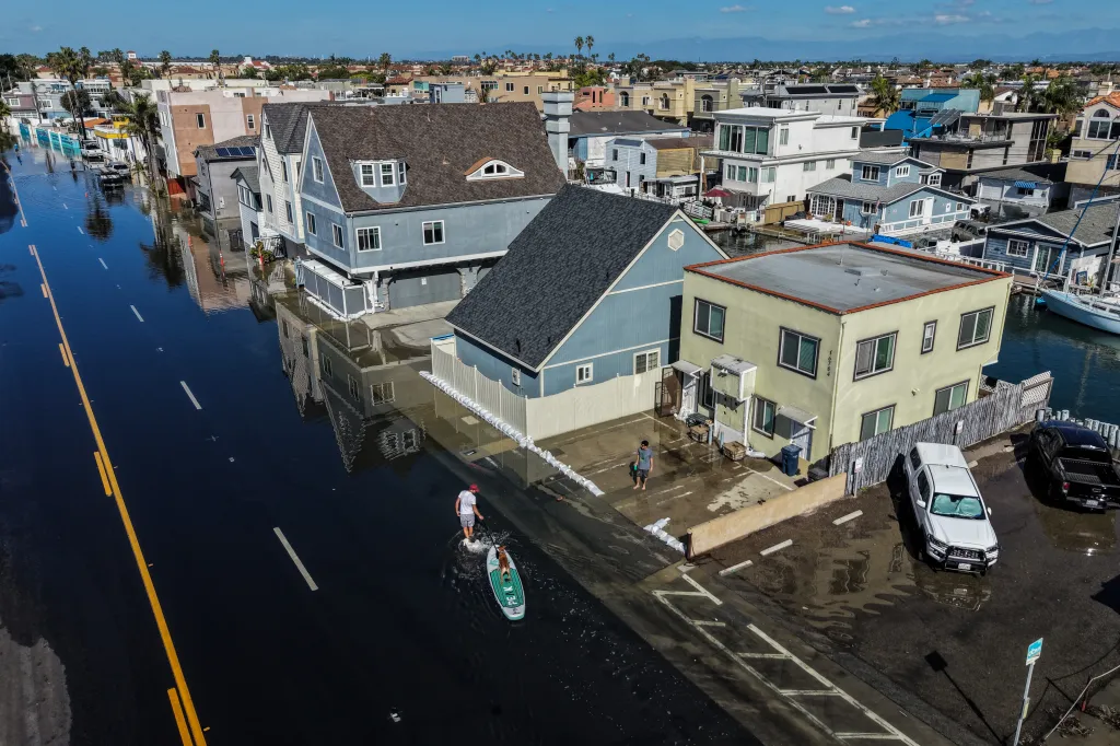 A man pulls his paddleboard with a dog on it through floodwaters on a street in Huntington Beach, California.