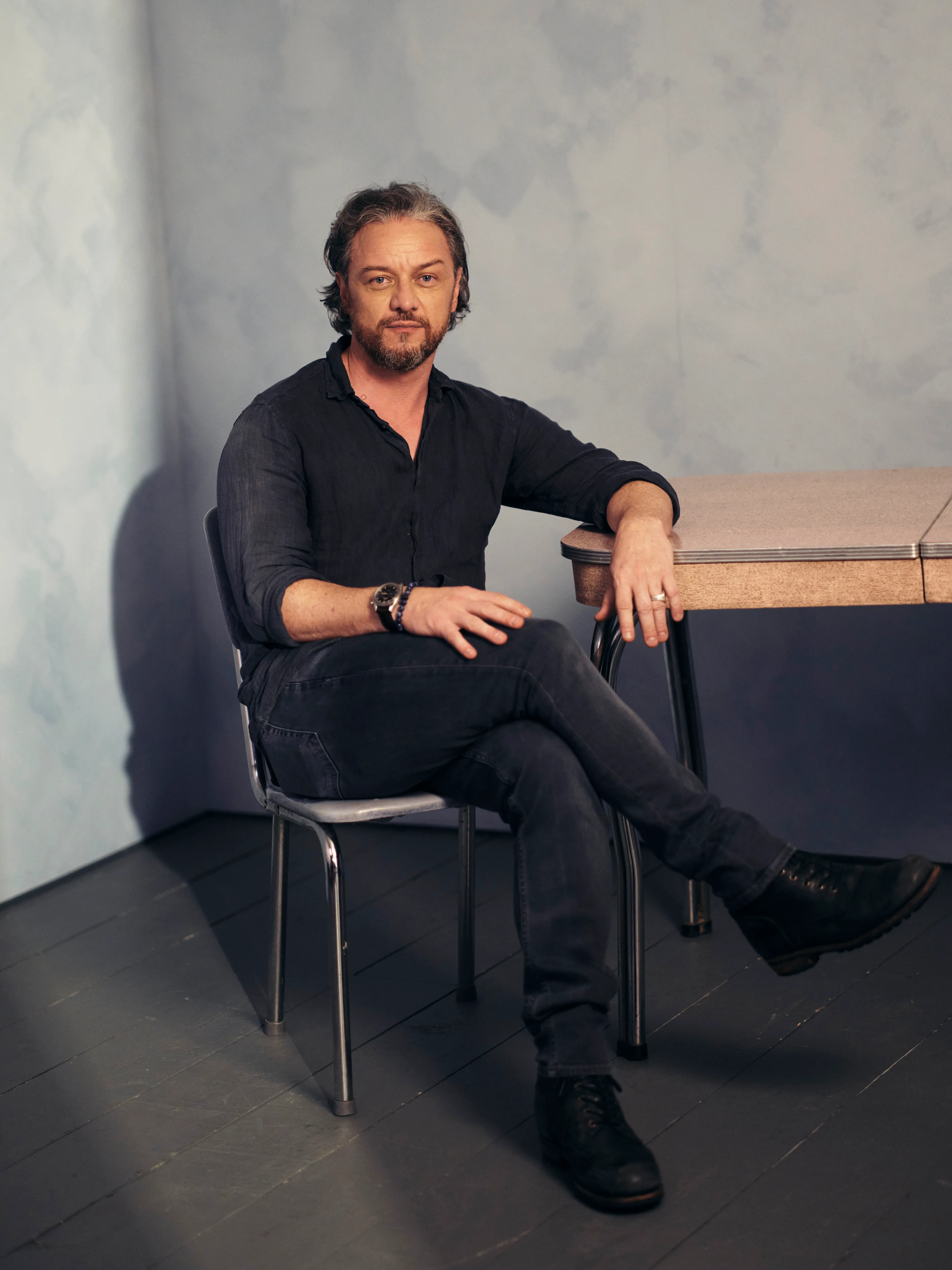 James McAvoy sits on a chair in a portrait studio.