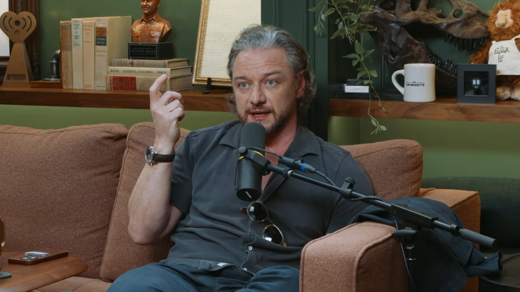 James McAvoy sitting on a brown couch talking into a microphone on a podcast.