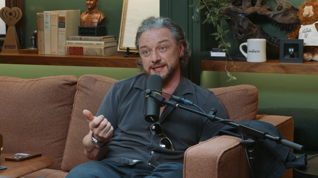 James McAvoy sitting on a couch and speaking into a microphone during an interview.