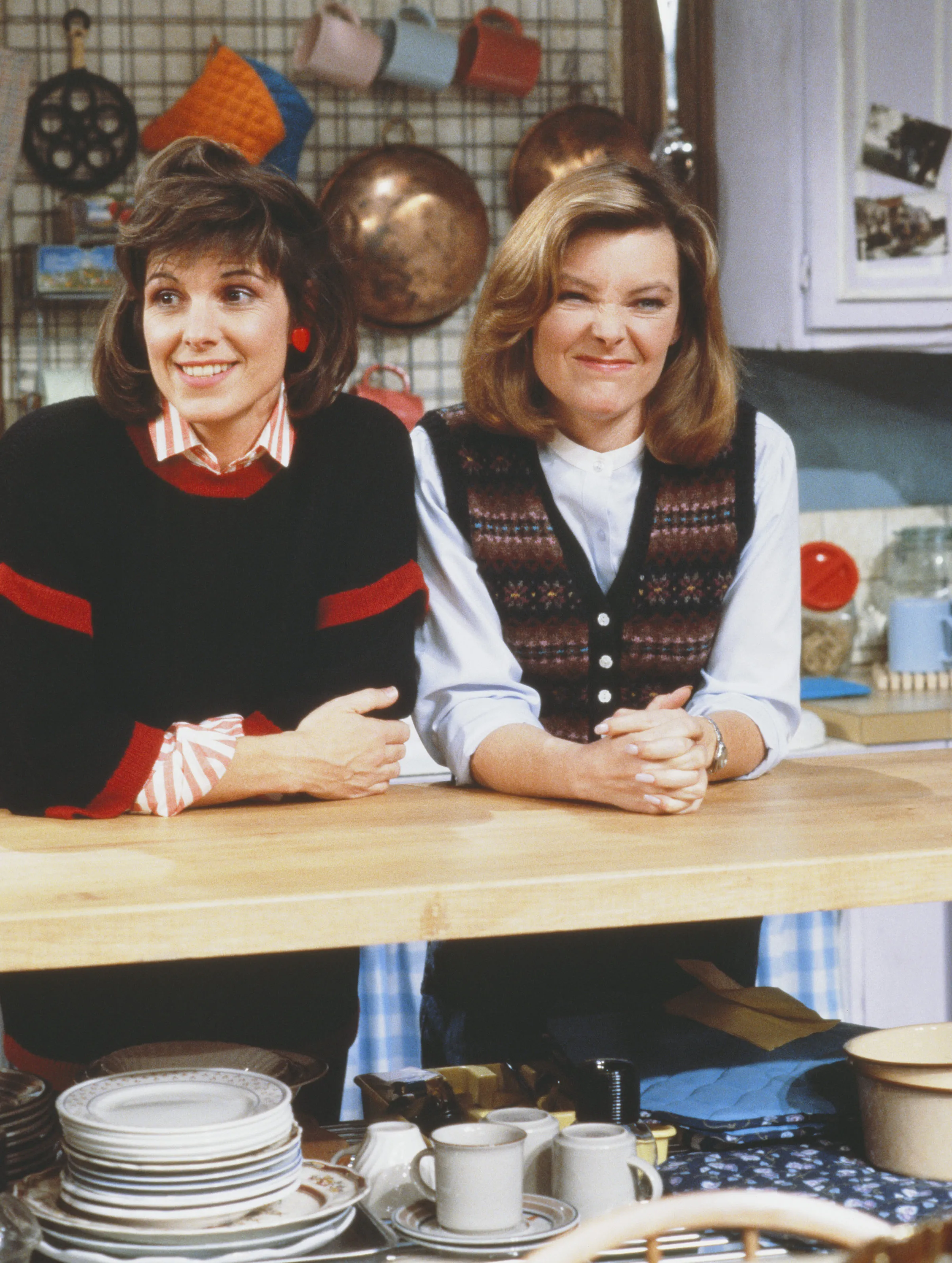Susan Saint James and Jane Curtin lean against a kitchen counter in a still from the sitcom 'Kate & Allie.'