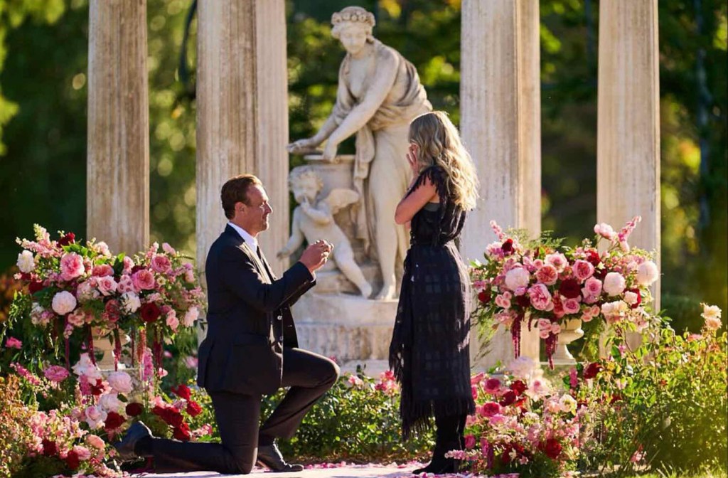 Jason Segel proposing to Kayla Radomski in a garden with pillars and floral arrangements.
