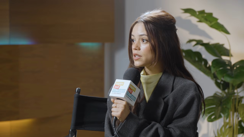 Jenna Ortega holding a Happy Sad Confused microphone while being interviewed.