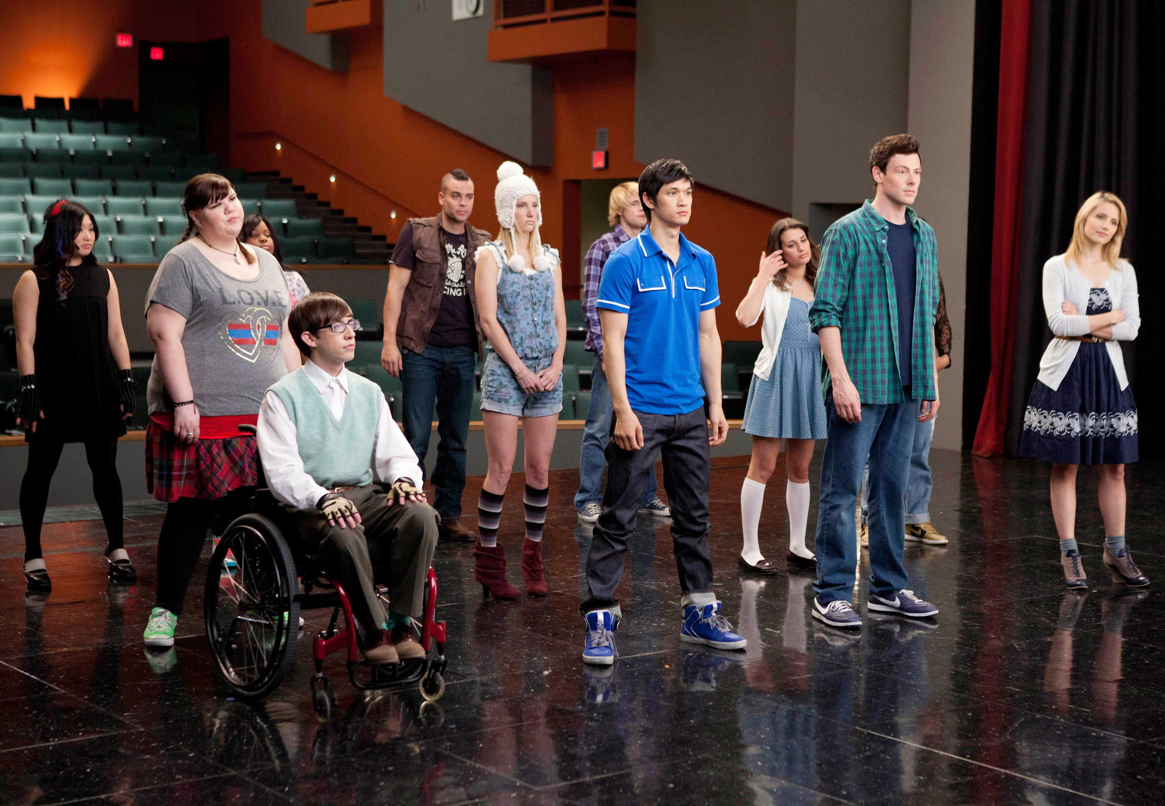 Cast of the television show Glee standing on an auditorium stage.