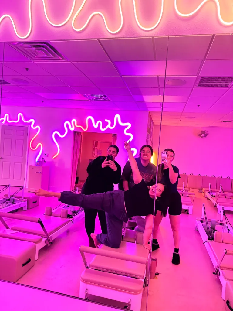 Jenny Voo posing in the front of a fitness studio with pink neon lights.