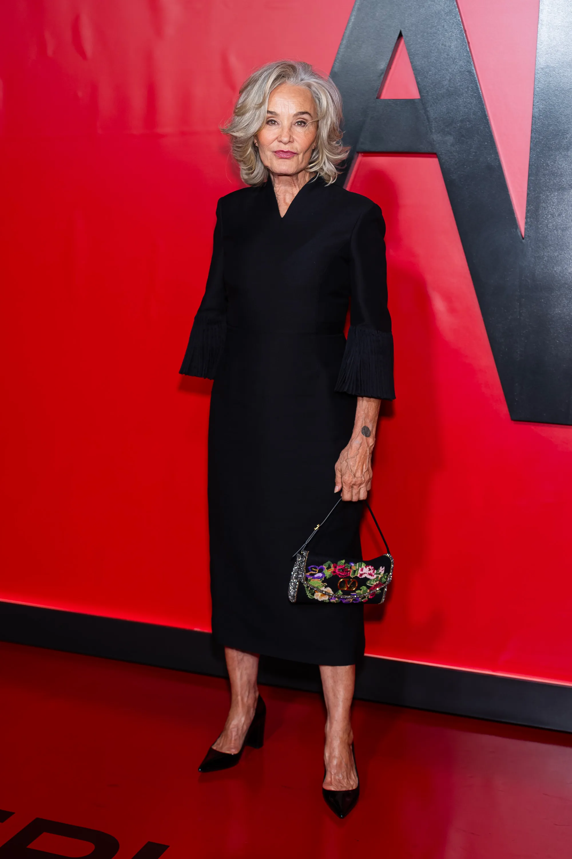 Jessica Lange in a black dress with pleated sleeves, holding a small embroidered handbag at FX's 
