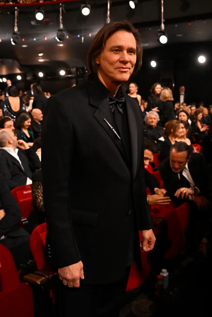 Jim Carrey in a black tuxedo standing in an audience.
