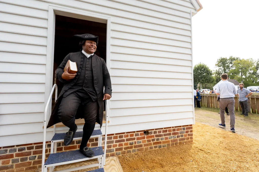 Joe Feaster, dressed in 18th-century attire as pastor Gowan Pamphlet, steps out of the First Baptist Church of Williamsburg carrying a book during its rededication ceremony.