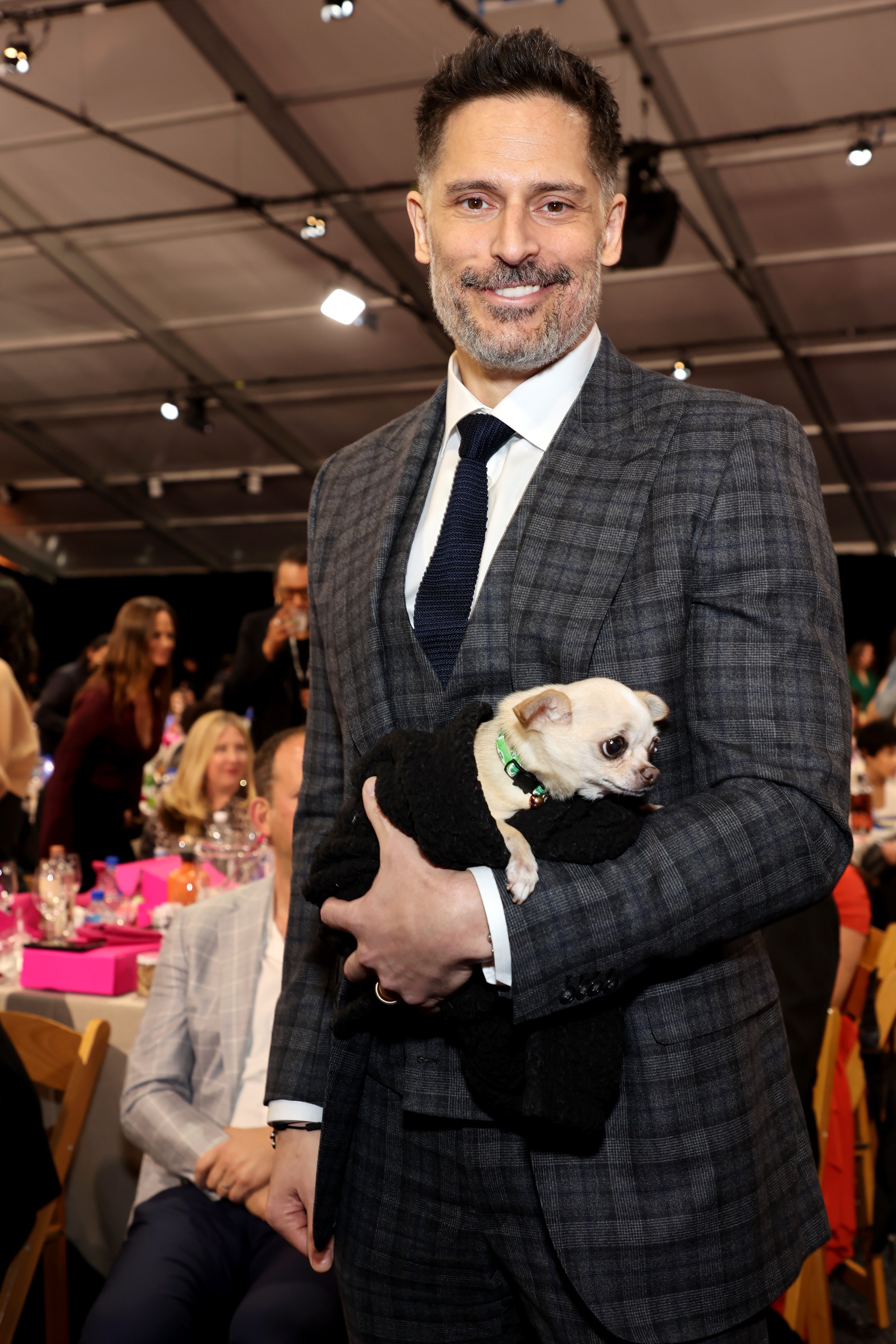Joe Manganiello holding a small dog in a black sweater.