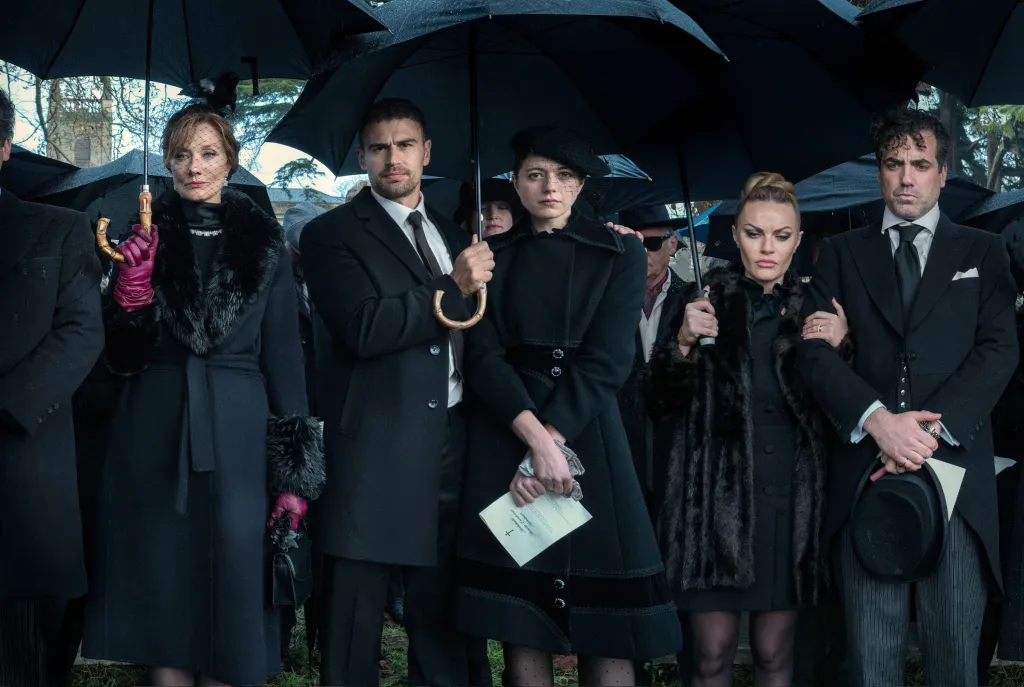 The cast of The Gentlemen in black mourning attire, holding black umbrellas at a funeral.