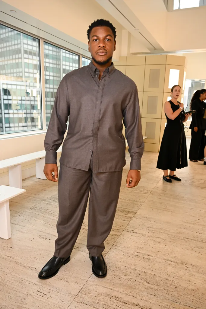 John Boyega attends the COS fashion show wearing a grey button-up shirt and matching trousers.