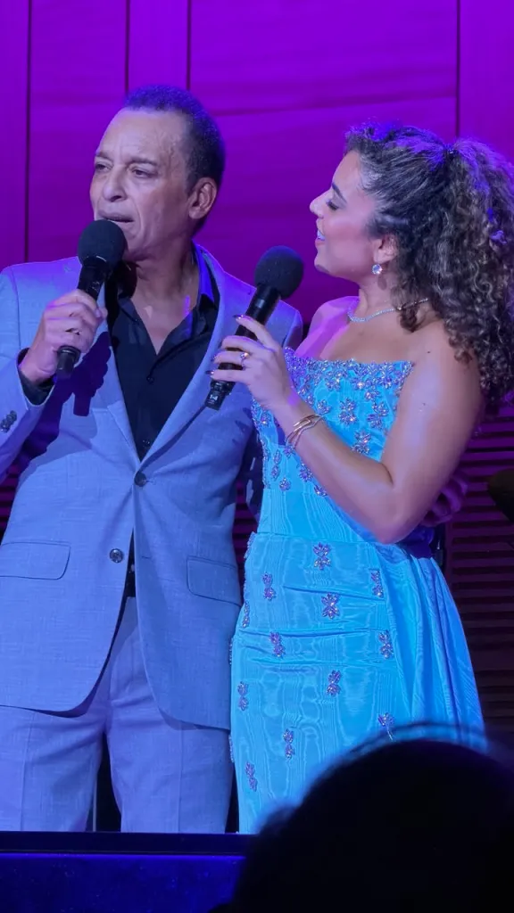 Jon Secada and his daughter Mikaela Secada singing into microphones on stage.