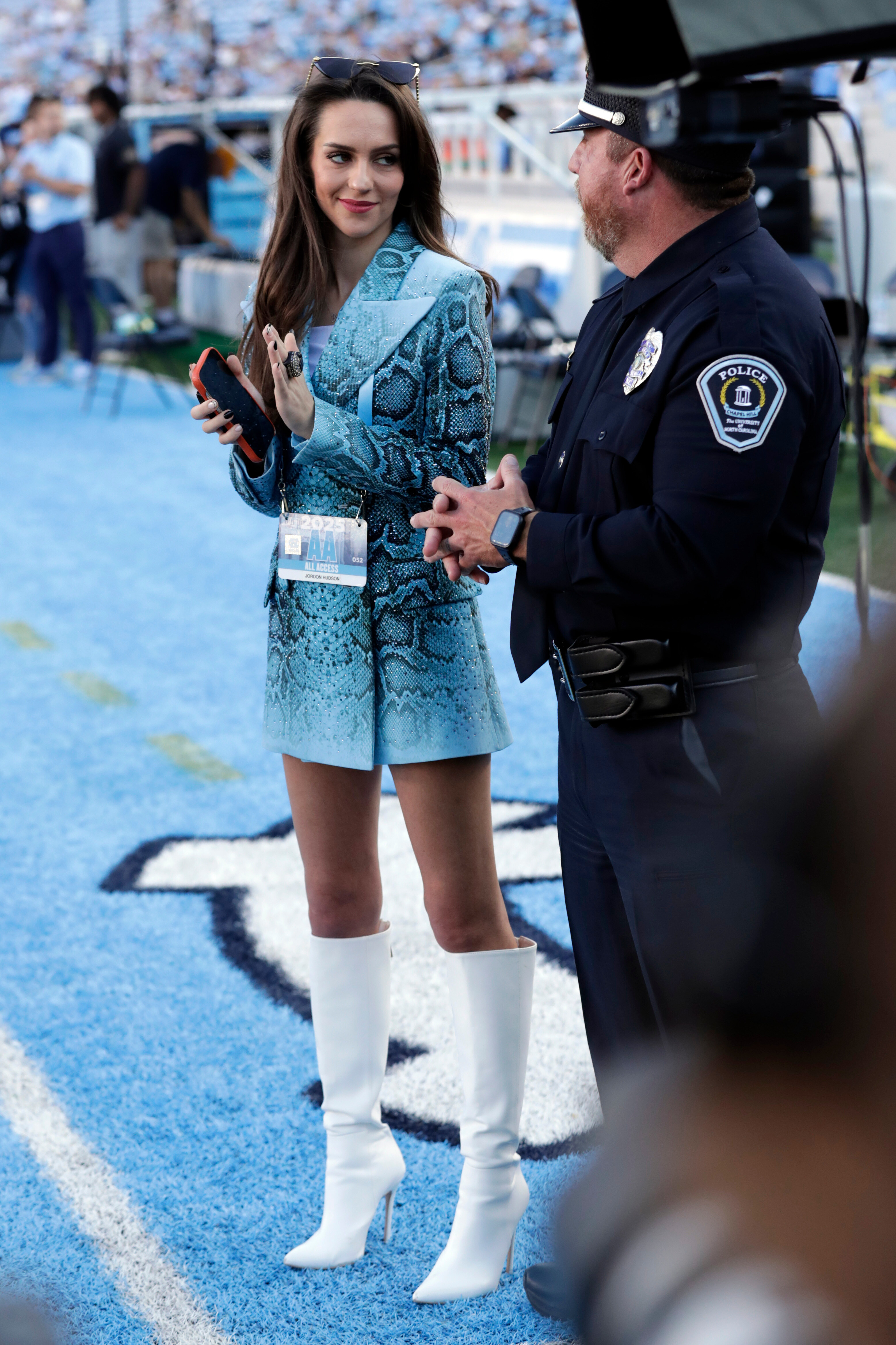 Jordon Hudson stands on the sideline next to a police officer on the field before a football game.