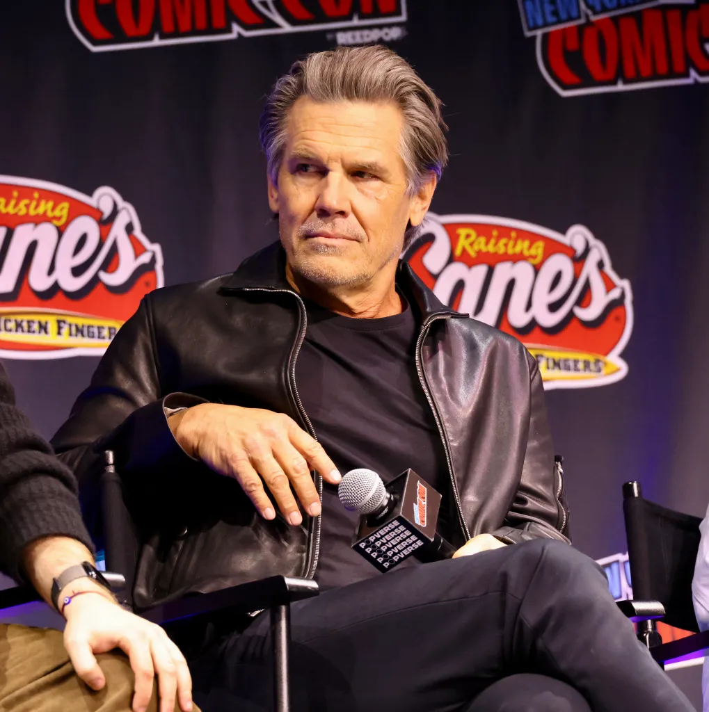 Josh Brolin wearing a black leather jacket and speaking at a panel.