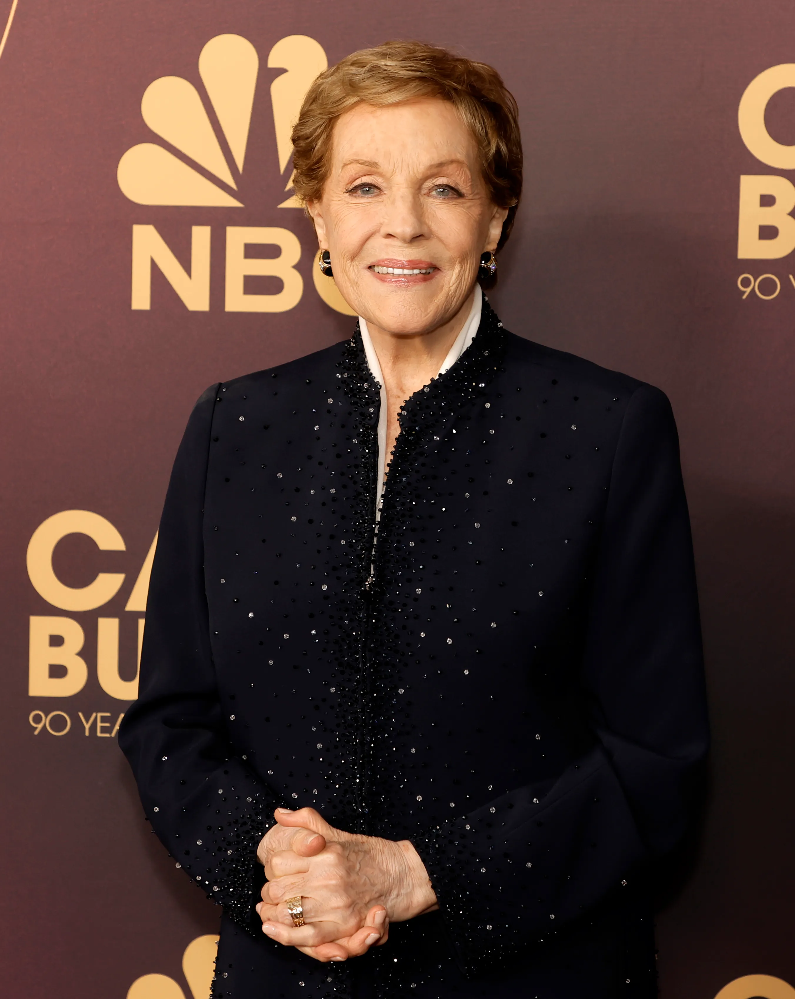 Julie Andrews smiles in front of an NBC background.