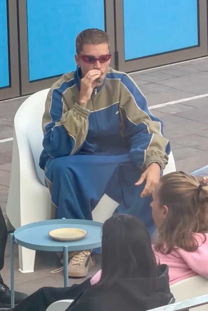 Justin Bieber wearing a blue tracksuit and sunglasses smokes a cigar while seated outdoors in Seoul, South Korea.